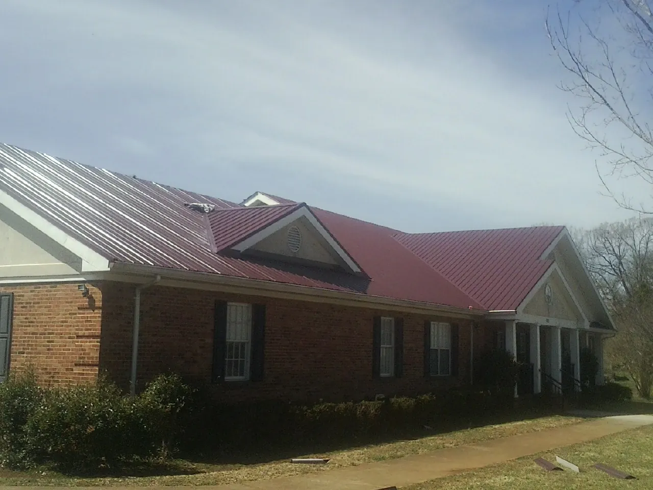 Red metal roof with gabled entries on a long brick building, from a Hail Damage Roof Repair job in Groveland