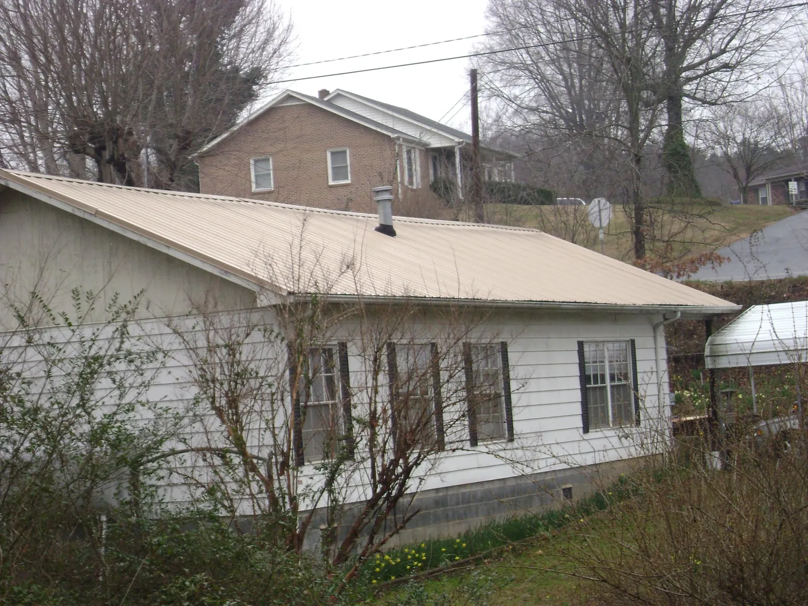 Tan metal roof on a white sided house set into a hillside — Commercial Roofing by Roofing Brothers in Groveland