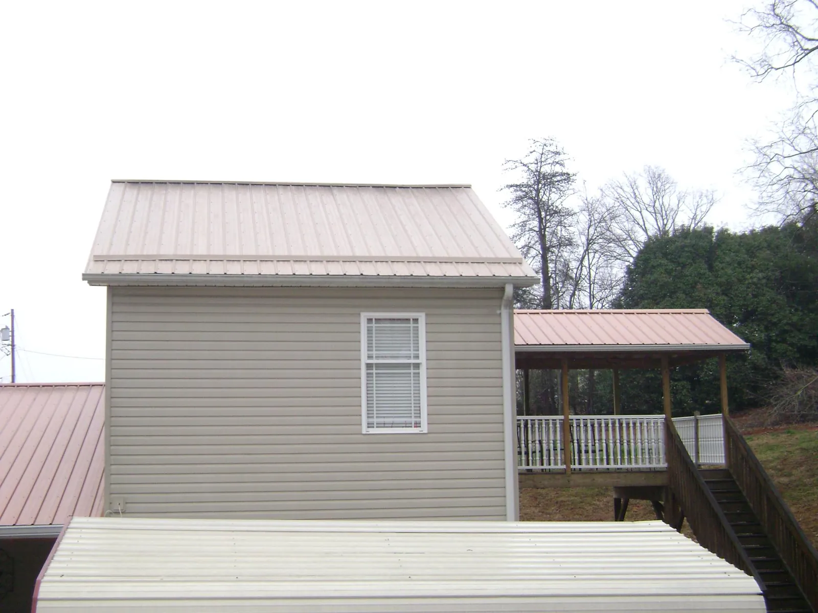 Tan metal roofs on a two story addition and attached porch, from a Roof Replacement job in Groveland
